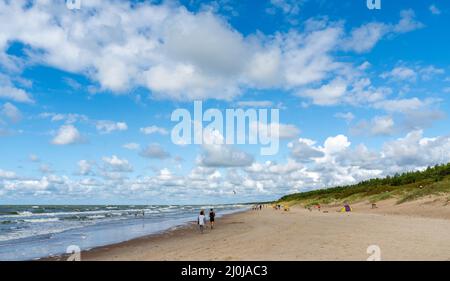 La gente gode di una giornata estiva su una idilliaca spiaggia di sabbia bianca senza fine con un oceano tranquillo e dolci onde e dune di sabbia Foto Stock