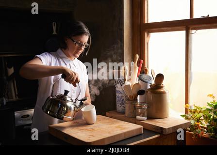 La cosa migliore dopo una lunga giornata. Scatto di una giovane donna attraente che fa una tazza di tè nella sua cucina. Foto Stock