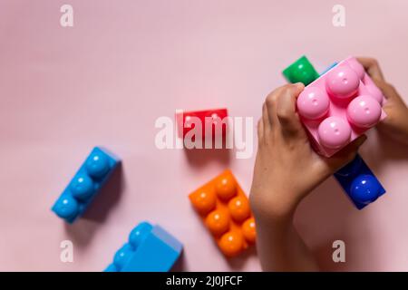 Vista dall'alto sulle mani dei bambini che giocano con mattoni di legno colorati sullo sfondo del tavolo bianco.edificio Kid con forme geometriche. Foto Stock