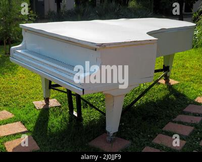 Un antico pianoforte bianco di legno si erge su un prato verde nel parco. Decorazioni in stile parco Foto Stock
