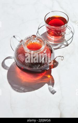 Tè di frutta con mele e timo e miele in teiera di vetro e tazza su sfondo bianco con ombre dure Foto Stock