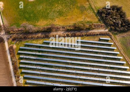 Un sistema solare fotovoltaico montato a terra con pannelli solari, cespugli, piste agricole e prati in Germania da una vista con droni Foto Stock
