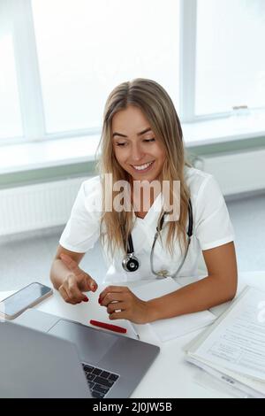 Medico femmina effettuare videochiamata online consultare il paziente sul portatile. Assistente medico giovane donna terapista videoconferenza a web camera. Foto Stock