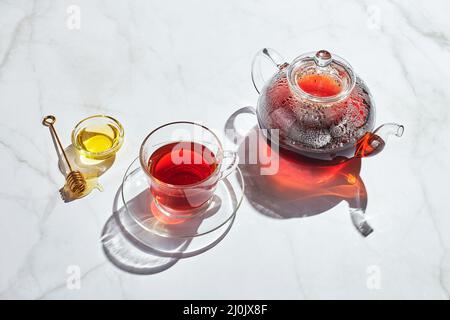 Tè di frutta con mele e timo e miele in teiera di vetro e tazza su sfondo bianco con ombre dure Foto Stock