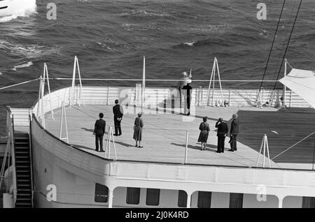 Il QE2 torna a casa a Southampton. Union Jacks è festooned sulle automobili, drappeggiato sulle spalle, ondulato sui bastoni. Southampton dà il benvenuto a "Three Cheers" al QE2 lussuoso liner trasformato in trooper di ritorno dalla guerra. A bordo è il suo prezioso carico, i 700 sopravvissuti della HMS Coventry, ardent e Antelope, affondati nella battaglia per le Falklands. Nella foto, l'incontro del QE2 con Royal Yacht Britannia, la Regina Madre che ondeggiava dal ponte di poppa. 11th giugno 1982. Foto Stock