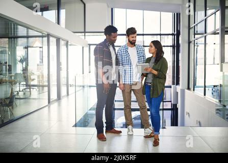 Realizzare idee innovative. Foto di tre giovani designer che lavorano su un tablet digitale in un ufficio moderno. Foto Stock