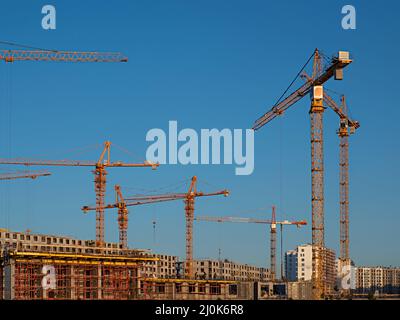 Alcune gru a torre sullo sfondo del cielo blu e lavoratori industriali e costruttori con hardhat in uniforme versare calcestruzzo in cantiere Foto Stock