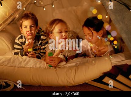 Campeggio in camera da letto. Colpo di tre bambini piccoli in una coperta forte bolle soffianti. Foto Stock