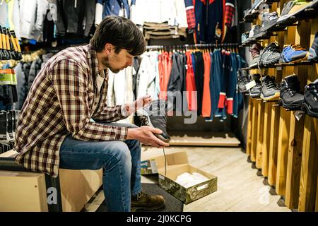 Uomo che acquista in un negozio all'aperto. Maschio acquistare scarponi da montagna. Negozio di articoli sportivi, scarpe da trekking selezionate. Acquisto cliente di Foto Stock