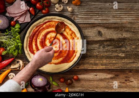 Pasta di pizza cruda e deliziosa con souce rosso sul tavolo di legno Foto Stock