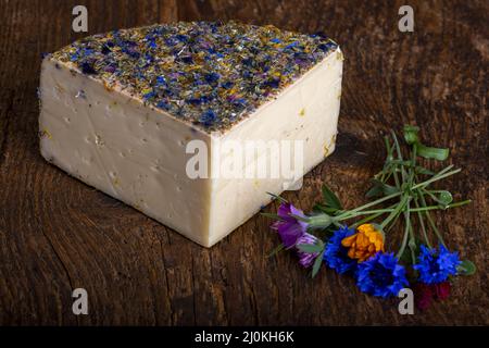 Formaggio di montagna con fiori su legno Foto Stock