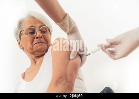 Donna caucasica anziana pensionato paura di aghi riceve un vaccino e si prende cura della sua salute. Sfondo bianco. Foto di alta qualità Foto Stock