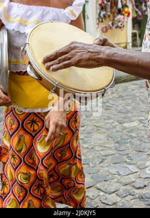 Giocatore di tamburello con una donna in abiti tipici che ballano sullo sfondo Foto Stock