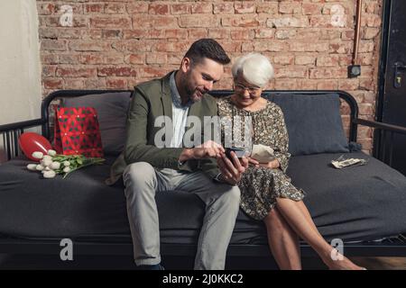 la madre anziana caucasica e il figlio di mezza età celebrano la giornata della madre seduta su un divano e guardando vecchie fotografie e ricordi. Foto di alta qualità Foto Stock