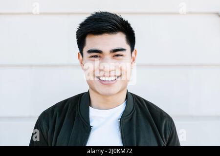 Il giovane uomo asiatico sorride con sicurezza alla macchina fotografica mentre si trova sulla strada della città Foto Stock