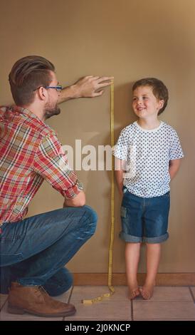 Guarda quanto sei cresciuto. Colpo di padre che misura l'altezza dei suoi ragazzi contro un muro a casa. Foto Stock