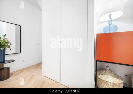 Porta d'ingresso e sala di una casa residenziale con una sponda rossa, cestino di vimini e un vaso con una pianta accanto ad uno specchio Foto Stock