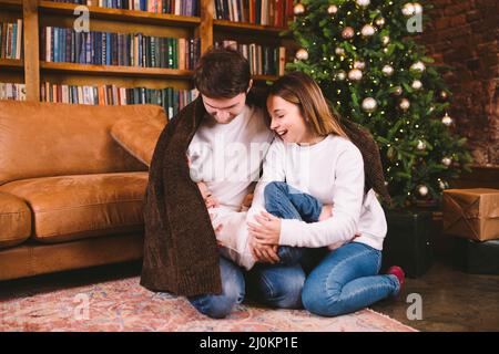 Una famiglia felice la vigilia di Natale sul pavimento sotto coperta vicino all'albero di Natale in serata a casa. Famiglia che passa il tempo di Natale Foto Stock