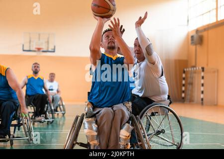 I veterani della guerra disabili hanno mescolato le squadre di pallacanestro di età e di corsa in carrozzina che giocano un match di addestramento in una sala della palestra di sport. Handicap Foto Stock