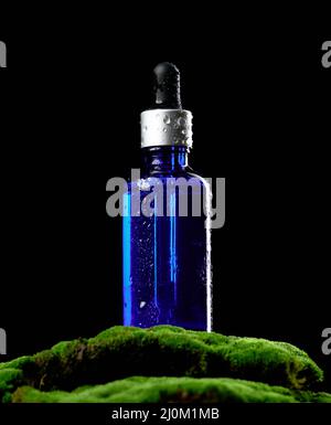 Flacone in vetro blu con portapipette su muschio verde, sfondo nero. Cosmetici SPA marchio mockup Foto Stock