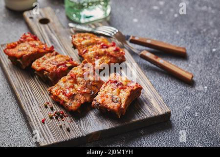 Costolette di maiale cotte alla griglia con spezie su tagliere di legno su sfondo scuro. Concetto di cibo americano. Foto Stock