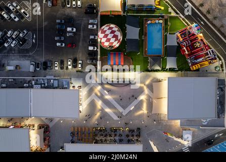 Vista aerea del drone dei parcheggi con auto e parco divertimenti di notte. Centro commerciale luminoso e affollato Foto Stock