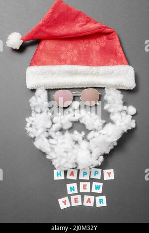 Cappello Santa in velluto con baffi da occhiali da sole con barba e l'iscrizione Felice anno nuovo su sfondo grigio. Tessera di Capodanno Foto Stock