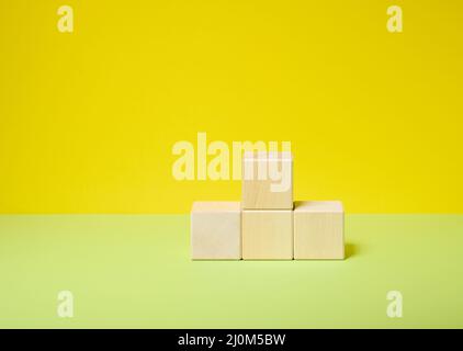 Cubetti di legno impilati in un piedistallo su sfondo giallo-verde, un luogo per visualizzare qualsiasi prodotto cosmetici, cibo, bevande Foto Stock