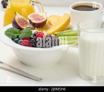 Piatto completo con farinata d'avena e frutta, succo appena spremuto in un decanter trasparente in vetro, tazza di caffè su un tavolo bianco. Healt Foto Stock