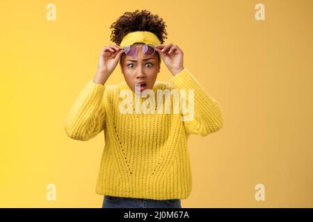 Che heck. Scioccato stordito confuso afro-americano elegante ragazza moderna in fasciatesta maglione take-off occhiali da sole allargano gli occhi sorp Foto Stock