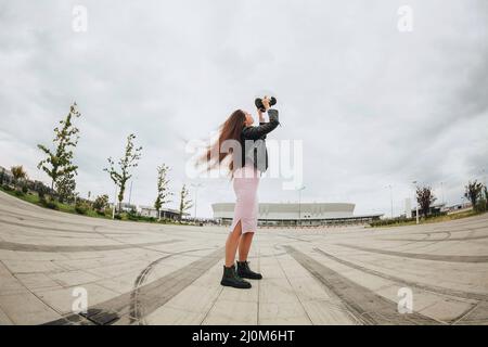 Giovane ragazza attraente biker indossa casco di sicurezza per bicicletta mentre si trova in piedi allo stadio vuoto all'aperto Foto Stock