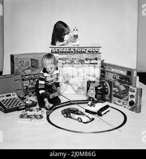 Un ragazzo e una ragazza con una selezione di giocattoli per bambini per Natale. Dicembre 1980. Foto Stock