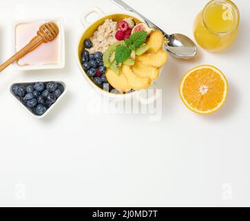 Piatto con farina d'avena e frutta, mezzo succo d'arancia maturo e spremuto di fresco in un decanter trasparente in vetro, miele in una ciotola sopra Foto Stock