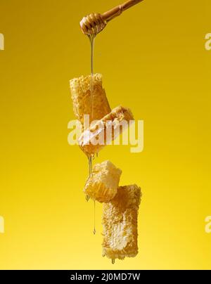 Versare il miele dolce trasparente da un bastone di legno su un nido d'ape di cera. Sfondo giallo Foto Stock