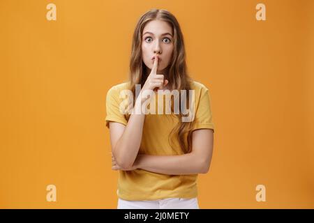 Shh tenere tranquillo durante il gioco. Giovane donna seria e determinata, con capelli ondulati, con gesto shush e indice di folgore Foto Stock