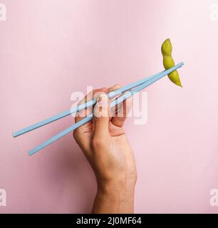 Tenere a mano i bacchetti con il fagiolo di edamame Foto Stock