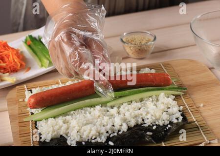Gimbap è un alimento coreano a base di riso bianco al vapore e vari altri ingredienti, arrotolati in GIM. Preparare il gimbab, mettere la salsiccia Foto Stock