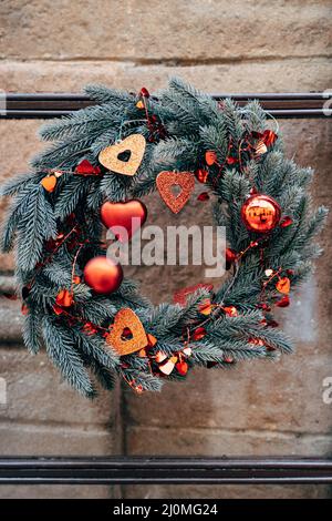 Corona di Natale di rami di abete con decorazioni natalizie rosse su un muro di pietra. Foto Stock