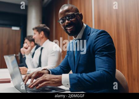 African american uomo d'affari nero seduto al tavolo con laptop in ufficio squadra gente sfondo. Foto Stock