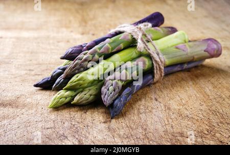 Mazzo di asparagi verdi e viola crudi da vicino su un rustico asse di legno con spazio copia Foto Stock