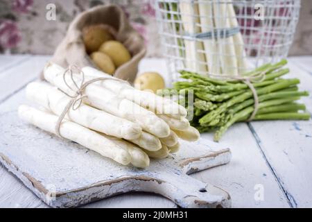 Asparagi verdi e bianchi crudi con patate sullo sfondo offerti come primo piano su un rustico tavolo in legno shabby chic Foto Stock