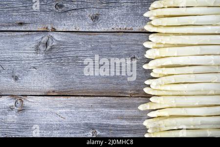 Asparagi bianchi grezzi bordati in fila su un vecchio rustico asse di legno come primo piano con spazio di copia a sinistra Foto Stock