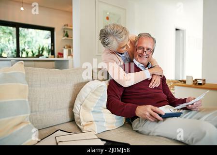 Sarete ricompensati bene per la spesa sotto il preventivo. Colpo di una donna anziana che abbraccia il suo marito mentre lui risolve il loro preventivo mensile. Foto Stock