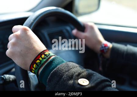 Braccialetto fai-da-te con motivo a bandiera Rasta con simbolo di pace sul polso. Mani che tengono il volante nella vettura. Foto Stock