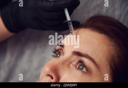 Primo piano del cosmetologo che fa iniezione nella fronte di una donna. La giovane donna ottiene le iniezioni facciali di bellezza nel salone. Faccia invecchiamento, ringiovanimento un Foto Stock