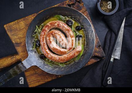 Tradizionale salsiccia italiana fritta salsiccia di carne all'aperto servita con erbe e olive come vista dall'alto in una padella di ghisa Foto Stock
