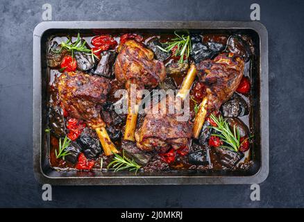 Tradizionale stinco di agnello brasato a cottura lenta in salsa di vino rosso con melanzane e pomodori serviti come vista dall'alto in una forma di supporto Foto Stock