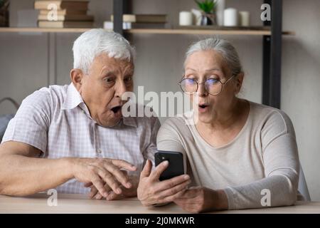 I nonni aprono il gawp della bocca allo schermo del telefono cellulare, leggano le notizie unbelievable Foto Stock