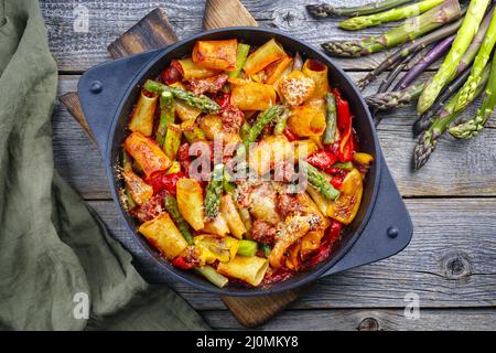 Tradizionale pasta italiana arrostita mezzi paccheri rigati con salsiccia salsiccia con punte di asparagi verdi in salsa di pomodoro servito a. Foto Stock