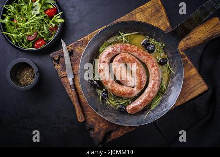 Tradizionale salsiccia italiana fritta salsiccia di carne all'aperto servita con insalata di rucola e olive come vista dall'alto in una padella di ghisa Foto Stock